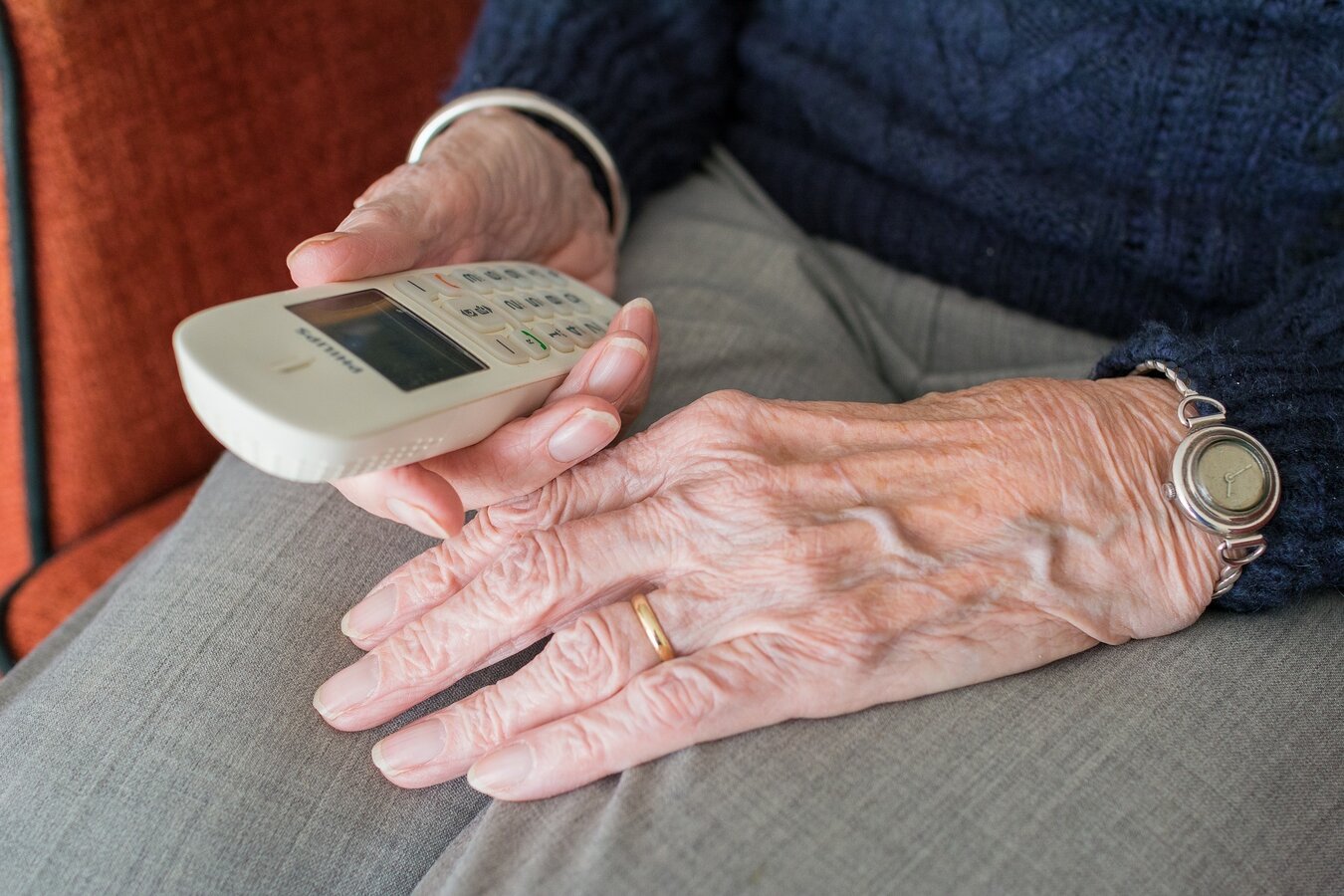 Zdjęcie przedstawia starszą osobę trzymającą telefon w dłoni 