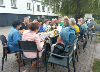 Zdjęcie przedstawia siedzących Seniorów przy stole