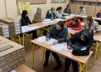 zdjęcie przedstawia rodziców siedzących w szkolnych ławkach 